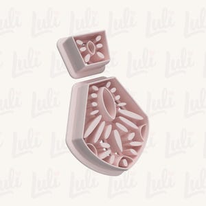 May include: A light pink, two-piece cookie cutter set. The larger piece is a stylized flower shape with oval and petal cutouts. The smaller piece is a square with a similar floral design. The background has a repeating pattern of the word "Luli".