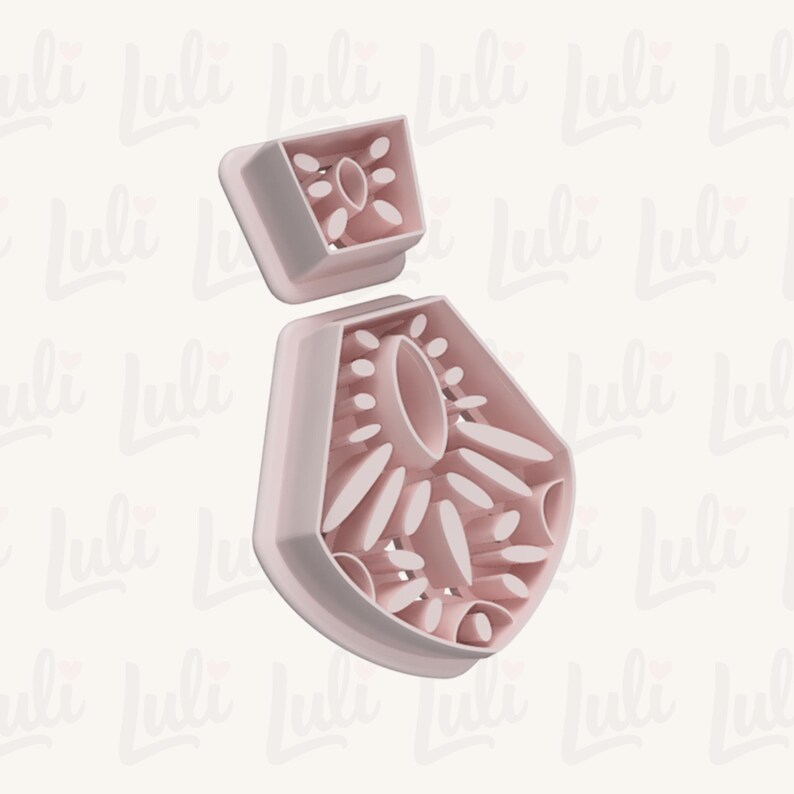 May include: A light pink, two-piece cookie cutter set. The larger piece is a stylized flower shape with oval and petal cutouts. The smaller piece is a square with a similar floral design. The background has a repeating pattern of the word "Luli".