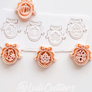 May include: A set of peach-colored plastic cookie cutters featuring oval frames with bows, containing designs of a squirrel, pumpkin, maple leaf, and mushroom. The cutters are shown alongside impressions made in white dough, with the text @LuliCutters.
