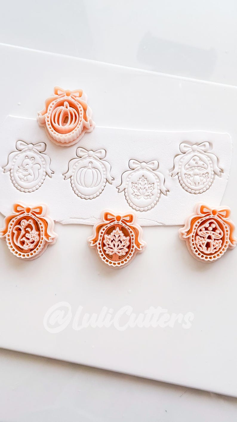 May include: A set of peach-colored plastic cookie cutters featuring oval frames with bows, containing designs of a squirrel, pumpkin, maple leaf, and mushroom. The cutters are shown alongside impressions made in white dough, with the text @LuliCutters.