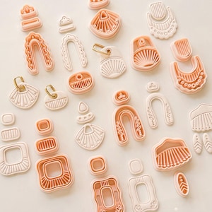 Può includere: Una collezione di formine per argilla in plastica color pesca in varie forme geometriche e organiche, inclusi archi, quadrati e disegni a ventaglio. Alcune formine presentano intricate texture interne come linee, punti e creste per impronte dettagliate.