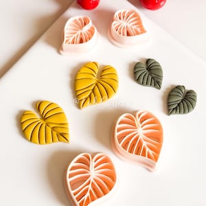 May include: A selection of leaf-shaped craft tools and finished leaves in various colours. The tools are light pink, and the leaves are yellow and green. A red berry branch is in the background.