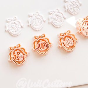 May include: A collection of oval-shaped cookie cutters featuring embossed designs of a squirrel, a pumpkin, a maple leaf, and a mushroom, each topped with a bow. The cutters are white and peach-colored, with the text @LuliCutters visible at the bottom.