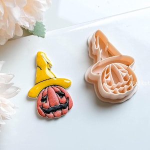 Peut inclure: Un ensemble de découpoirs sur le thème d'Halloween représentant une citrouille souriante portant un chapeau de sorcière jaune. La citrouille est rouge avec des détails noirs. À côté, un découpoir assorti de couleur pêche clair. Le fond est blanc.