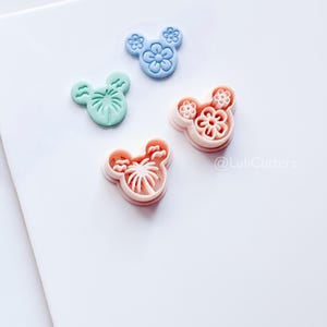Peut inclure: Quatre emporte-pièces colorés en forme de tête de souris avec des motifs floraux et de palmiers. Les emporte-pièces sont dans des tons pastel de bleu, vert et rose. Le texte "@LuliCutters" est visible dans le coin inférieur droit.