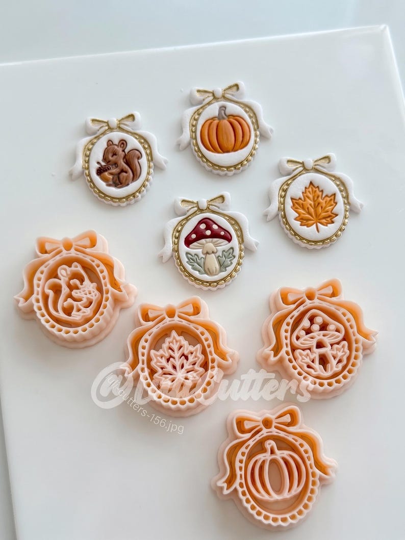 May include: A collection of seven oval-shaped cookie cutters and matching embossed cookies featuring autumn themes. The designs include a squirrel with an acorn, a pumpkin, a maple leaf, and a mushroom, all framed by a decorative bow and border.