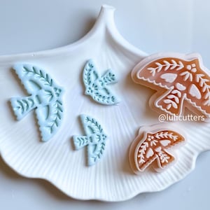 May include: A set of four cookie cutters in the shape of birds. Two of the cutters are light blue and two are light pink. The cutters have intricate designs and are perfect for making decorative cookies.