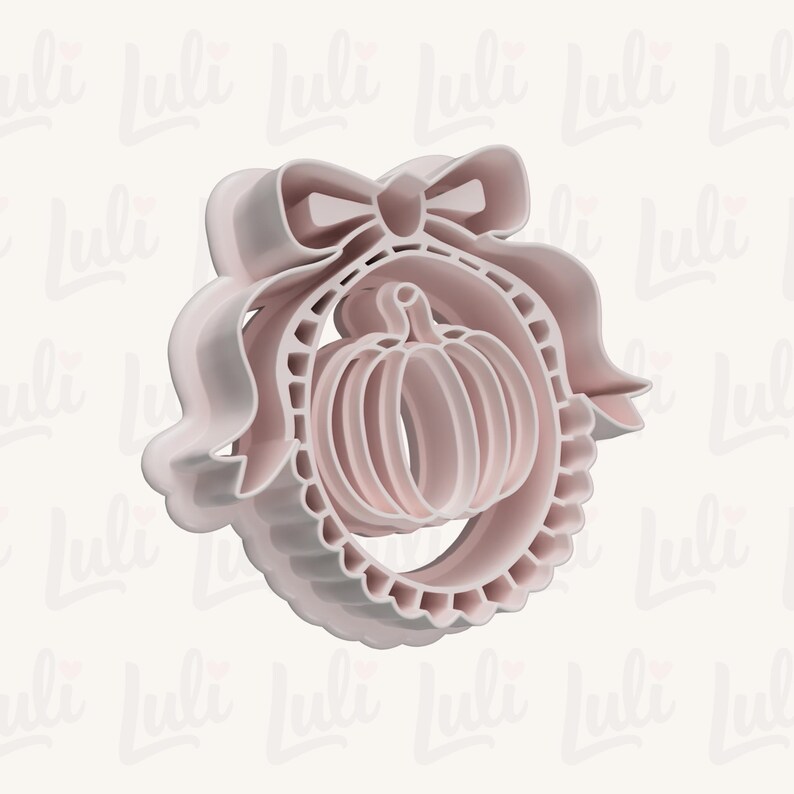 May include: A light pink plastic cookie cutter featuring a central pumpkin shape enclosed within a circular frame that is decorated with a ruffled edge and topped with a large, prominent bow detail at the top of the circular structure.