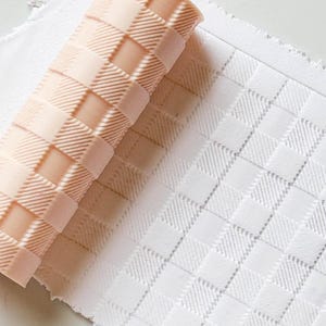 Peut inclure: Un rouleau à pâtisserie pêche clair avec un motif à carreaux texturé, à côté d'une feuille de matériau blanche avec le même motif à carreaux. Le rouleau à pâtisserie est partiellement déroulé, révélant le motif imprimé.