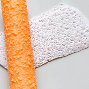 Könnte beinhalten: Eine orangefarbene, strukturierte Rolle mit einer weißen, strukturierten, pastenartigen Substanz darauf.