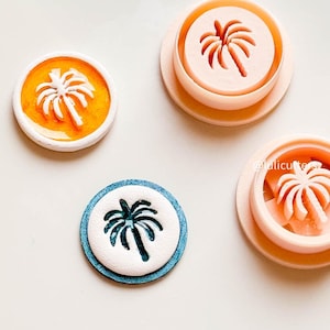 May include: Palm tree-shaped cookie cutters and embossed cookies in orange, blue, and white. The cutters are light pink. The cookies have a tropical theme. The image is on a white background.