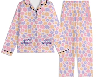 May include: A two-piece pyjama set with a floral pattern in pastel shades. The long-sleeved top has two pockets with the text "90's Night". The trousers have an elasticated waistband. Black trim outlines the collar, pockets, and cuffs.
