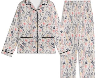 May include: A floral patterned pajama set in cream, with pink, blue, and yellow flowers and leaves. The long-sleeved top has a notched collar, two pockets, and black trim. The matching trousers have a relaxed fit.