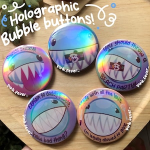 May include: Five circular holographic buttons featuring cartoon shark characters with sharp teeth. The buttons display text including "Sounds Sticky!", "you should throw a BEACH PARTY!", "Explain to daddy Bupple how bad thing?", and "made with all the love I'm legally allowed to give".