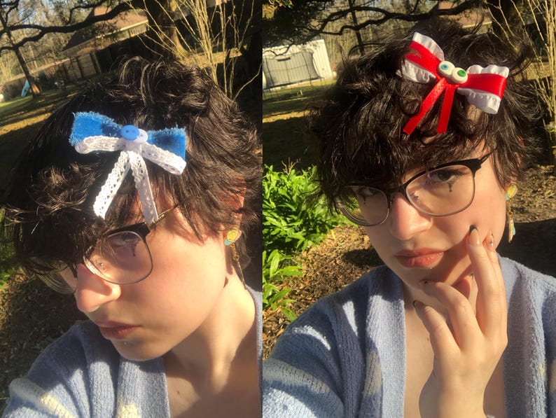 Pu&ograve; includere: Due fiocchi per capelli fatti a mano. Uno &egrave; blu con pizzo bianco e un bottone al centro. L'altro &egrave; rosso e bianco con accenti di occhi verdi. Entrambi sono attaccati a capelli scuri. La persona indossa occhiali e un cardigan azzurro.