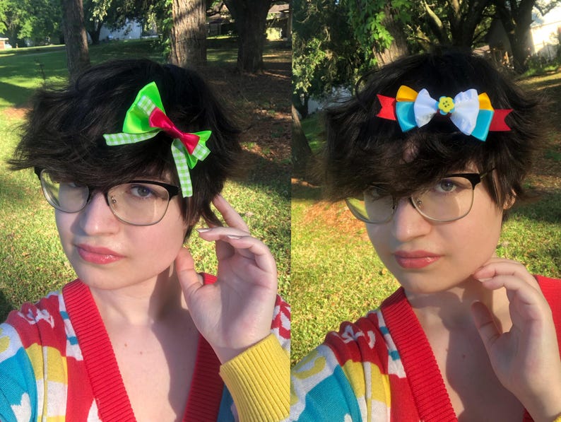 Pu&ograve; includere: Due immagini di una persona con occhiali e un cardigan colorato. La prima immagine mostra un fermaglio per capelli con fiocco verde e rosso. La seconda immagine mostra un fermaglio per capelli con fiocco con nastri gialli, blu e bianchi. Lo sfondo &egrave; un'area erbosa con alberi.