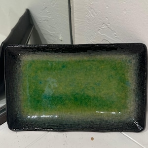 May include: Rectangular ceramic tray with a glossy finish. The tray features a vibrant green center, framed by a dark, almost black border. The surface has a crackle effect, adding texture. A decorative piece for serving or display.