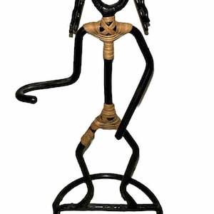 May include: Black metal sculpture of a person with a circular base. The figure has a looped head, long arms, and legs. The body is wrapped with tan-colored twine. The sculpture is a decorative item.