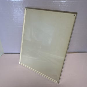 May include: A clear acrylic photo frame with a light beige backing. The frame has a rectangular shape and a thin, silver-colored border. The frame is designed to hold a photograph or artwork.