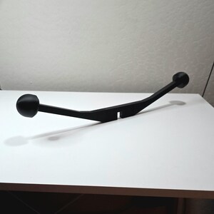 May include: A black, curved object with a ball on each end. The object has a flat, rectangular section in the middle. The item is sitting on a white surface.