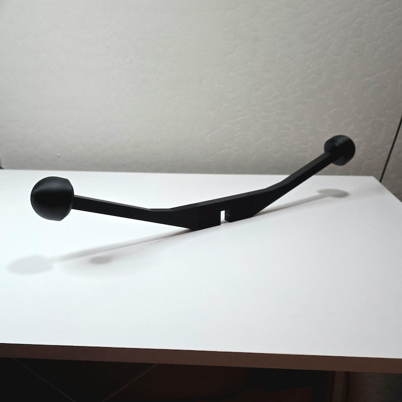 May include: A black, curved object with a ball on each end. The object has a flat, rectangular section in the middle. The item is sitting on a white surface.