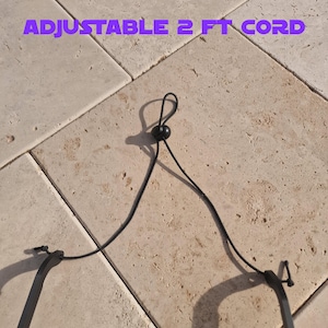 May include: A black adjustable cord with a sliding bead for adjustment. The cord is approximately 2 feet long. The text "ADJUSTABLE 2 FT CORD" is displayed in purple.
