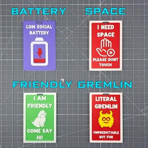 May include: Four colorful rectangular signs with humorous text. The signs read "LOW SOCIAL BATTERY", "I NEED SPACE", "I AM FRIENDLY", and "LITERAL GREMLIN". Each sign has a unique graphic and color scheme, including a battery, hand, dog, and gremlin.
