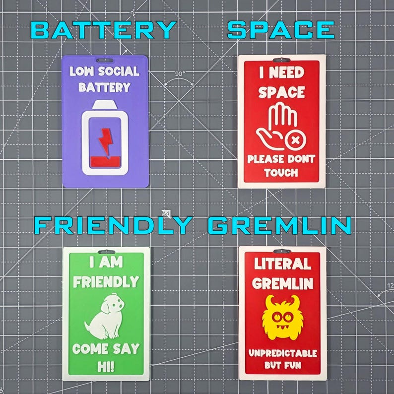 May include: Four colorful rectangular signs with humorous text. The signs read "LOW SOCIAL BATTERY", "I NEED SPACE", "I AM FRIENDLY", and "LITERAL GREMLIN". Each sign has a unique graphic and color scheme, including a battery, hand, dog, and gremlin.