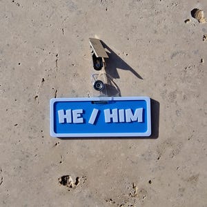Badge showing he/him on a tile background.