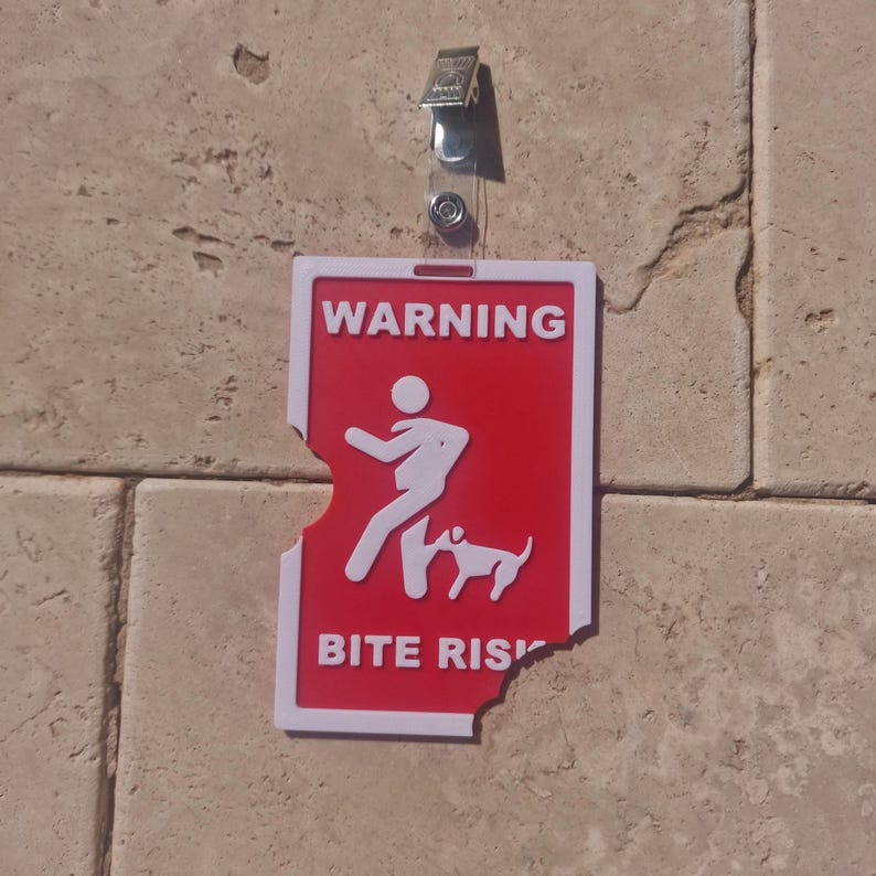 May include: A red and white warning sign with the text "WARNING BITE RISK" and a graphic of a person and dog. The sign is attached to a wall with a clear plastic clip.