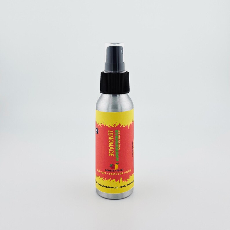 May include: A silver spray bottle with a black cap and a red and yellow label. The label reads "LEMONADE" in large, vertical letters. Below the word "LEMONADE" is a graphic of a lemon and strawberry. The bottle contains 50ml (1.7 fl oz).