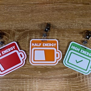 May include: Three badge reels with battery-shaped designs. The badges are red, orange, and green, labelled "Low Energy", "Half Energy", and "High Energy". Each badge has a white border and a retractable clip.