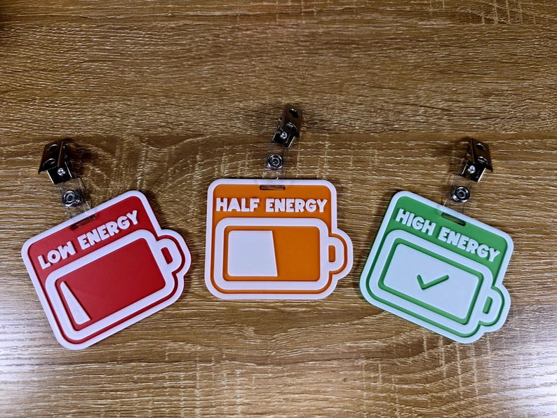 May include: Three badge reels with battery-shaped designs. The badges are red, orange, and green, labelled "Low Energy", "Half Energy", and "High Energy". Each badge has a white border and a retractable clip.