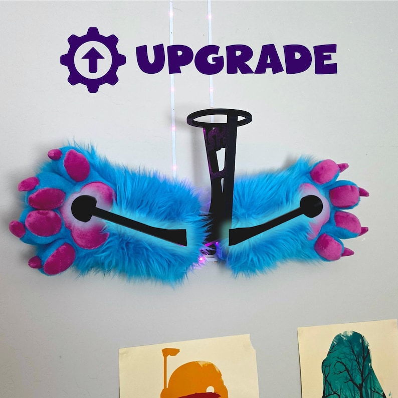 May include: A pair of blue and pink furry paw-shaped accessories with the word "UPGRADE" above them. The paws have pink pads and claws, and are connected by a black structure. The background is a white wall.