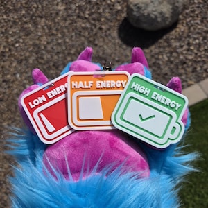 May include: Three energy level tags: red "Low Energy", orange "Half Energy", and green "High Energy". The tags have white borders and battery icons. They are attached to a furry, multi-coloured paw.