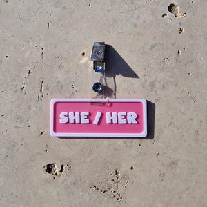 Badge showing she/her on a tile background.