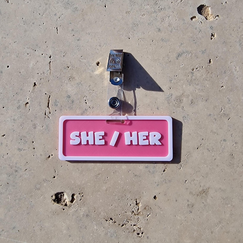 Badge showing she/her on a tile background.