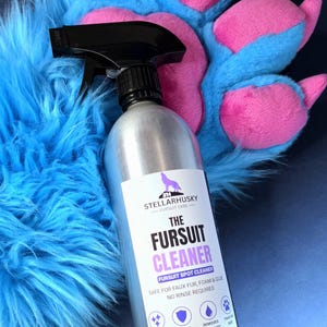 May include: A silver spray bottle with a black trigger nozzle featuring a white label that reads STELLARHUSKY FURSUIT CARE THE FURSUIT CLEANER FURSUIT SPOT CLEANER SAFE FOR FAUX FUR, FOAM & GLUE NO RINSE REQUIRED, positioned against blue faux fur.