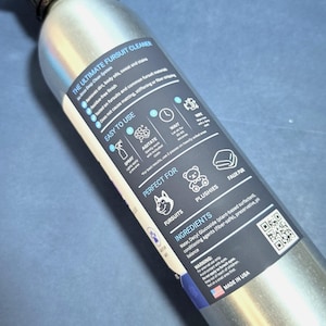 May include: A silver metal spray bottle featuring a dark blue label titled The Ultimate Fursuit Cleaner. The label includes instructions, a list of ingredients, a QR code, and icons representing fursuits, plushies, and faux fur materials.
