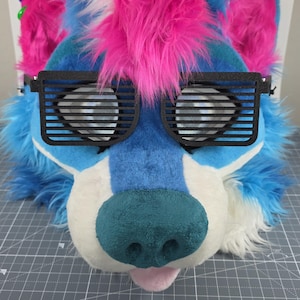 May include: A furry wolf head with blue, white, and pink faux fur. The wolf head has black shutter shades and a teal nose. The tongue is pink. The head is designed for cosplay or costume use.