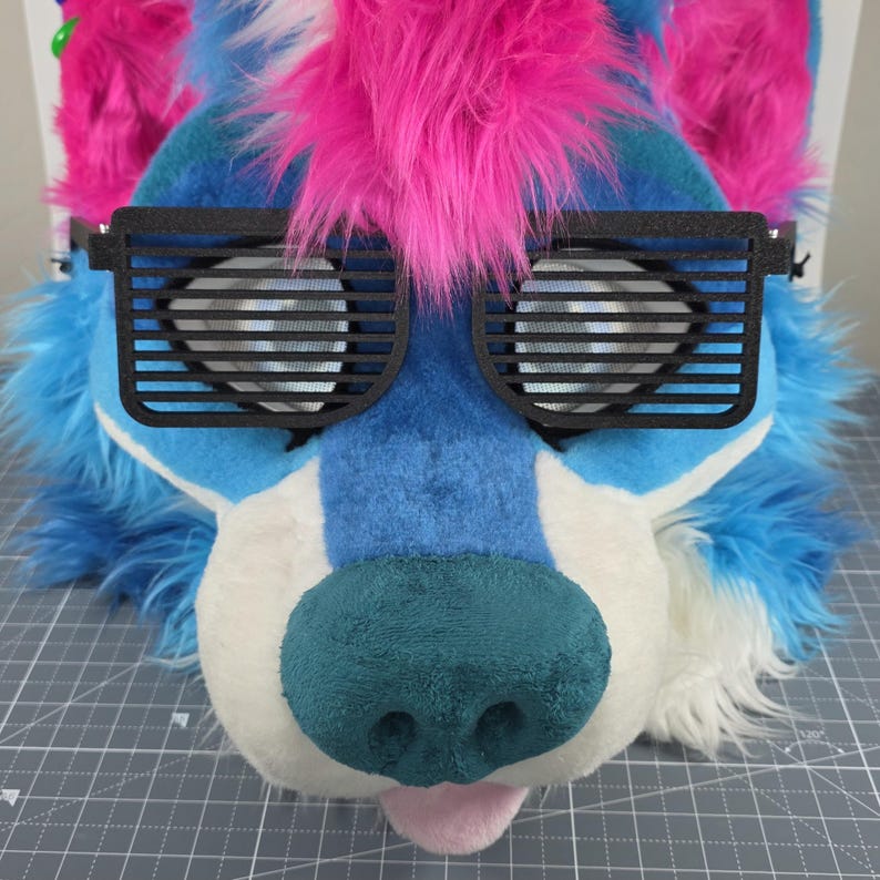 May include: A furry wolf head with blue, white, and pink faux fur. The wolf head has black shutter shades and a teal nose. The tongue is pink. The head is designed for cosplay or costume use.