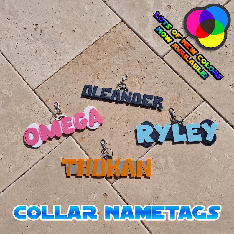 May include: A collection of colorful collar nametags with names like "Omega," "Oleander," and "Ryley." The tags are in various colors, including pink, blue, and orange, with a keychain attachment. Text in the image reads "Lots of New Colors Now Available!"