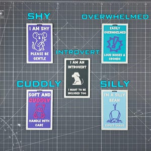 May include: A collection of rectangular, colorful badges with humorous phrases and illustrations. The badges include text like "I AM SHY," "OVERWHELMED," "INTROVERT," "CUDDLY," and "SILLY," each with a corresponding graphic.