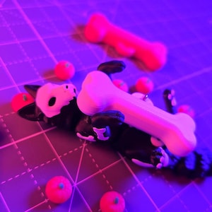 May include: A black and white dog figurine with a bone-shaped object on its body. Several small, red, round objects are scattered around the dog. A larger, red bone-shaped object is in the background. The objects are on a grid.