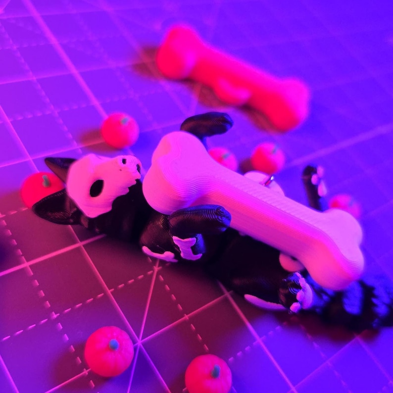 May include: A black and white dog figurine with a bone-shaped object on its body. Several small, red, round objects are scattered around the dog. A larger, red bone-shaped object is in the background. The objects are on a grid.