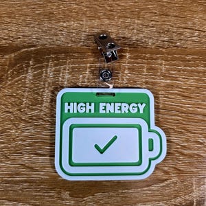 May include: A green and white badge with the words "HIGH ENERGY" and a battery icon with a checkmark. The badge has a metal clip for attachment.