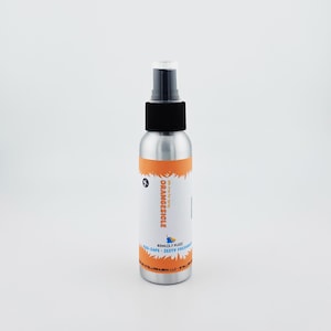 May include: A silver spray bottle with a black cap and a white label. The label features the word "ORANGESICLE" in orange, along with the text "AIR-SAFE ZESTY FRESHNESS". The bottle contains 2.7 fl oz of product.