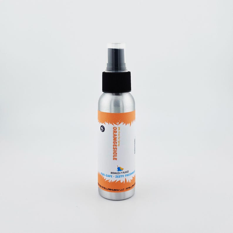 May include: A silver spray bottle with a black cap and a white label. The label features the word "ORANGESICLE" in orange, along with the text "AIR-SAFE ZESTY FRESHNESS". The bottle contains 2.7 fl oz of product.