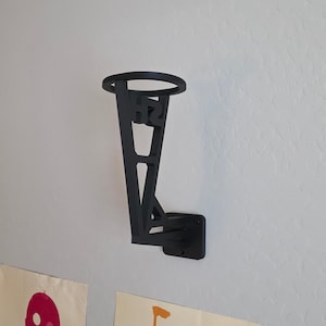 May include: Black wall-mounted basketball hoop with a circular rim and a rectangular base. The hoop has a unique design with the letters "HR" incorporated into its structure. It is mounted on a white wall.