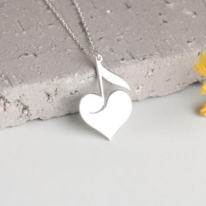 May include: A silver necklace with a heart-shaped pendant featuring a music note design.